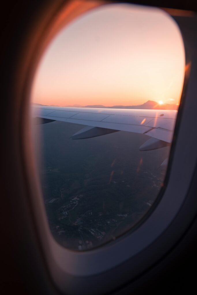 Airplane wing view through window during sunset, capturing a serene sky and landscape below.